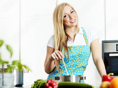 Photo: Young woman cooking in her kitchen, stiring in a pan Young woman cooking in her kitchen, stiring in a pan