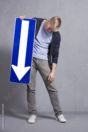 Photo: Sad man holding direction arrow sign pointing down. Sad man holding direction arrow sign pointing down.