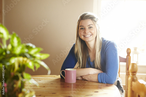 Photo: Young woman sitting at table smiling Young woman sitting at table smiling