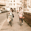 Two Beautiful Women Walking in the City with Bicycles and Bags