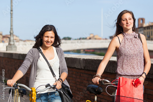 Photo: Two Beautiful Women Walking in the City with Bicycles and Bags Two Beautiful Women Walking in the City with Bicycles and Bags