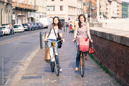 Photo: Two Beautiful Women Walking in the City with Bicycles and Bags Two Beautiful Women Walking in the City with Bicycles and Bags