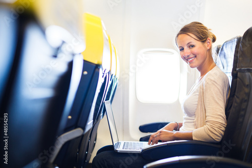 Photo: Young woman on her laptop computer on board of an airplane Young woman on her laptop computer on board of an airplane