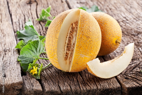 Photo: Melon with slices and leaves on a old wooden table. Melon with slices and leaves on a old wooden table.