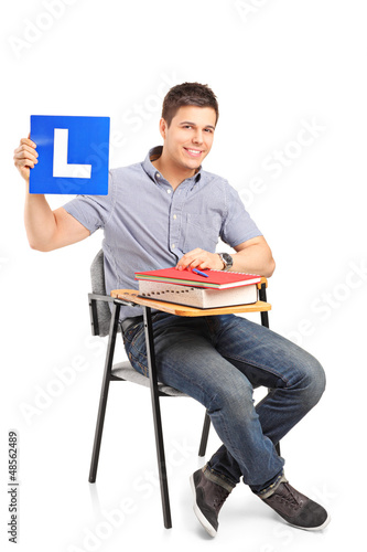 Photo: A student sitting on a school chair and holding a L plate A student sitting on a school chair and holding a L plate