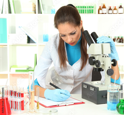 Photo: Young scientist looking into microscope in laboratory. Young scientist looking into microscope in laboratory.