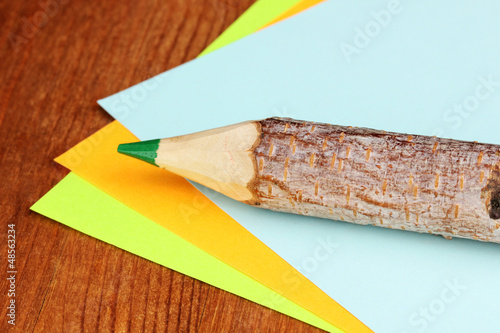 Photo: Colorful wooden pencil with sheets of paper on wooden table Colorful wooden pencil with sheets of paper on wooden table