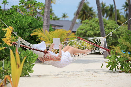 Photo: Woman relaxing in a hammock and reading a book on a beach Woman relaxing in a hammock and reading a book on a beach