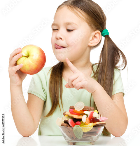 Photo: Little girl choosing between apples and sweets Little girl choosing between apples and sweets