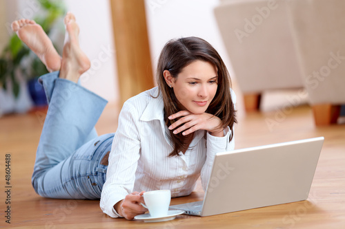 Photo: Young woman with laptop and a cup of coffee on the floor Young woman with laptop and a cup of coffee on the floor