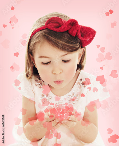 Photo: Little girl blowing heart confetti on pink background Little girl blowing heart confetti on pink background