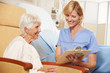 Nurse Taking Notes From Senior Female Patient Seated In Chair