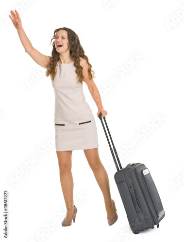 Photo: Young woman with wheels suitcase catching taxi Young woman with wheels suitcase catching taxi