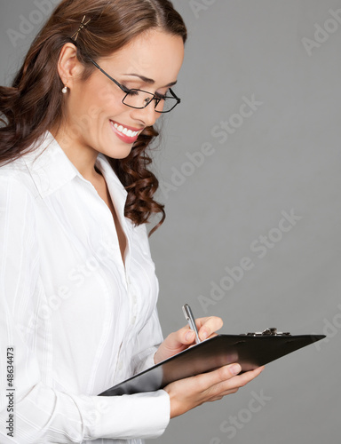 Photo: Businesswoman with clipboard writing, on gray Businesswoman with clipboard writing, on gray
