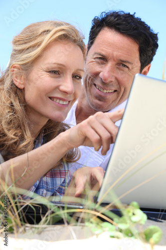 Photo: Couple looking at laptop outdoors. Couple looking at laptop outdoors.