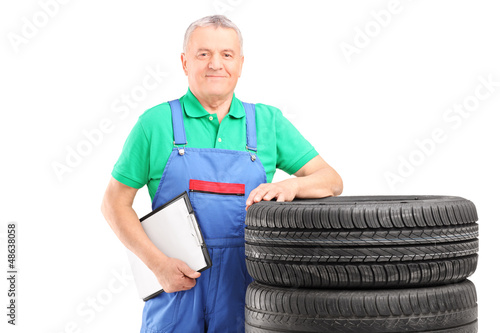 Photo: A mature worker posing on car tires with clipboard A mature worker posing on car tires with clipboard
