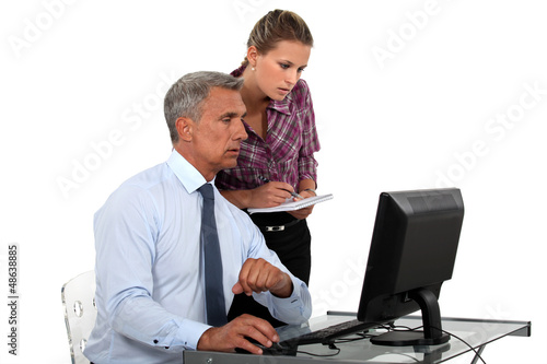 Photo: businessman in office with computer and young female assistant businessman in office with computer and young female assistant