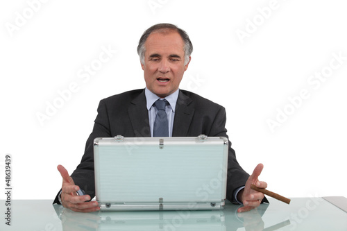 Photo: Senior businessman sat with cigar and metal briefcase Senior businessman sat with cigar and metal briefcase