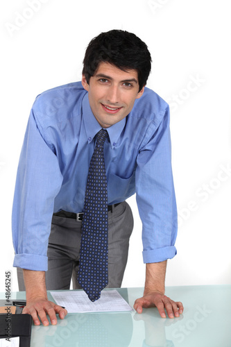 Photo: Young office worker leaning on his desk Young office worker leaning on his desk
