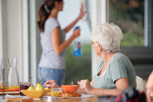 Photo: senior woman having breakfast with home care in the background senior woman having breakfast with home care in the background