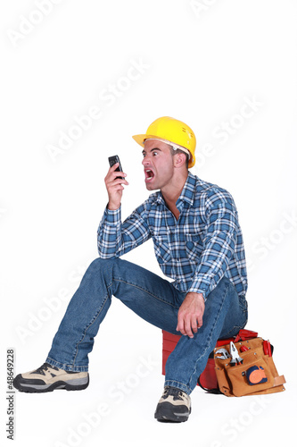 Photo: angry craftsman looking at his cell phone angry craftsman looking at his cell phone