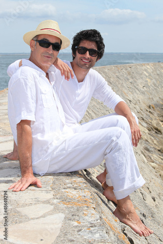 Photo: Grownup father and son sitting on a harbor wall Grownup father and son sitting on a harbor wall