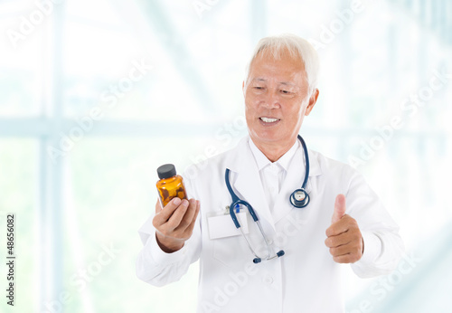 Photo: Thumb up Asian doctor holding bottle pills Thumb up Asian doctor holding bottle pills