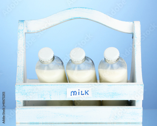 Photo: Milk in bottles in wooden box on blue background Milk in bottles in wooden box on blue background