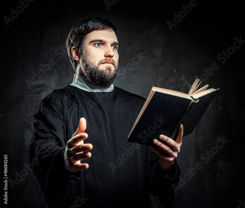 Photo: Priest with Prayer book against dark background Priest with Prayer book against dark background