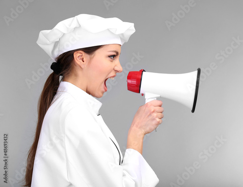 Photo: Portrait of young woman chef with megaphone on grey background Portrait of young woman chef with megaphone on grey background