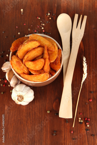 Photo: Appetizing village potatoes in bowl on wooden table close-up Appetizing village potatoes in bowl on wooden table close-up
