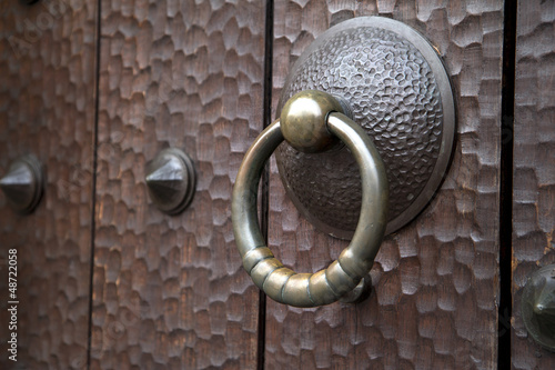 Photo: Old medieval brass knocker on antique dark wooden door Old medieval brass knocker on antique dark wooden door