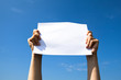 Hands holding clean white sheet paper over the sky