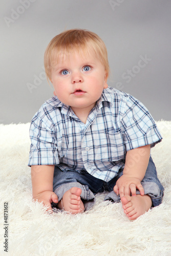 Photo: Little boy sitting on white carpet on gray background Little boy sitting on white carpet on gray background