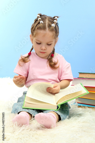 Photo: cute little girl with colorful books, on blue background cute little girl with colorful books, on blue background