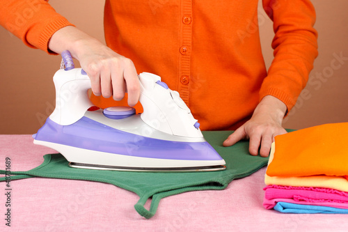 Photo: Young woman ironing her clothes, on brown background Young woman ironing her clothes, on brown background