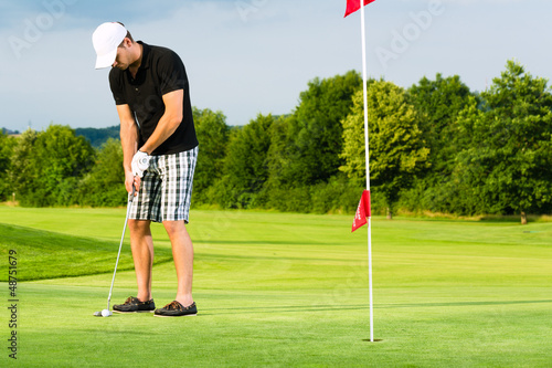 Photo: Young golf player on course putting to the hole Young golf player on course putting to the hole