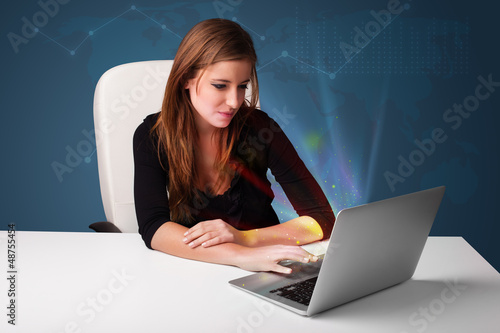 Photo: Beautiful woman sitting at desk and typing on laptop with abstra Beautiful woman sitting at desk and typing on laptop with abstra