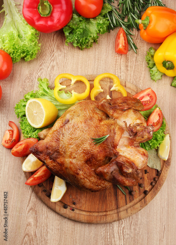 Photo: Whole roasted chicken with vegetables on plate, on wooden table Whole roasted chicken with vegetables on plate, on wooden table