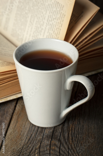 Photo: Cup of tea with old opened book on wooden table. Cup of tea with old opened book on wooden table.