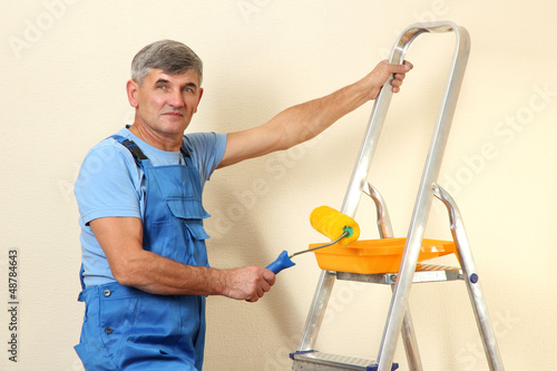 Photo: Male painter paints wall in room close-up Male painter paints wall in room close-up