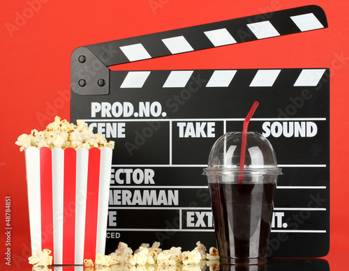 Photo: Movie clapperboard, cola and popcorn on red background Movie clapperboard, cola and popcorn on red background
