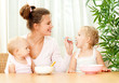 young mother feeding her two daughters from a spoon