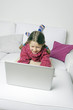 Kind liegt auf Couch und surft mit Laptop
