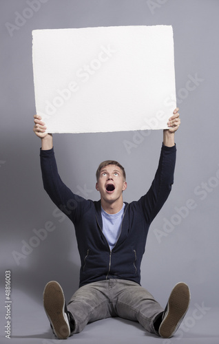 Photo: Astonished young man holding up empty panel. Astonished young man holding up empty panel.