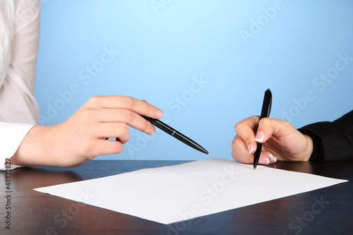 Photo: Two business partners signing document, on blue background Two business partners signing document, on blue background