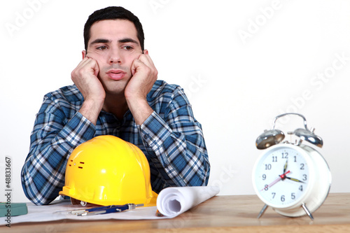 Photo: Construction worker with plans and an alarm clock Construction worker with plans and an alarm clock