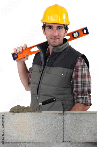 Photo: Stonemason standing before a wall and carrying a spirit level Stonemason standing before a wall and carrying a spirit level