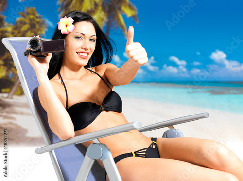 Photo: Happy woman with a video camera on beach Happy woman with a video camera on beach