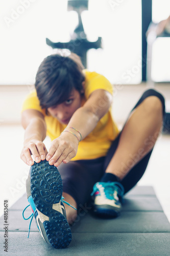 Photo: Young woman stretching her leg to warm up in the gym. Young woman stretching her leg to warm up in the gym.